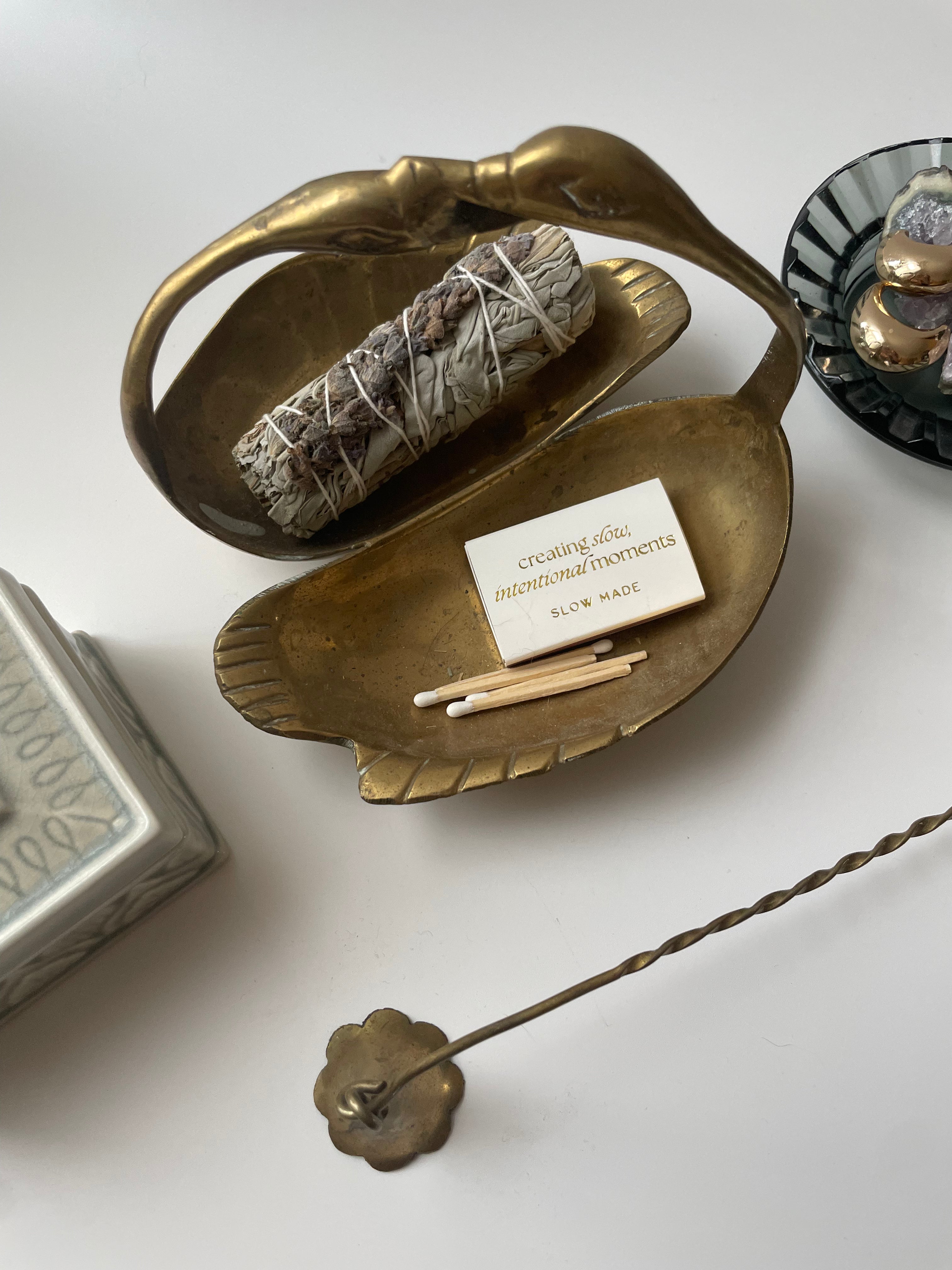 Brass incense holder with sage, matches, and a small card on a white surface.